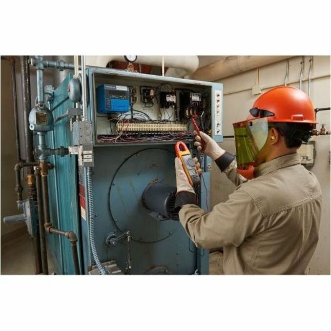 HVAC technician using Fluke 902 FC clamp meter to test industrial equipment while wearing safety gear