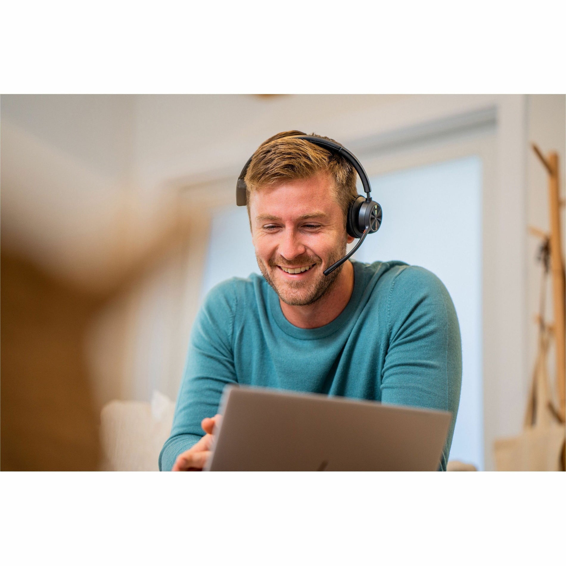 Person smiling while using laptop with Poly Voyager headset during video call-alternate-image7