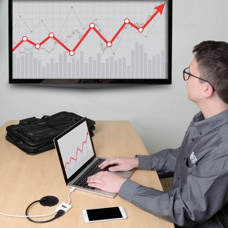 Professional using laptop connected to large monitor displaying financial charts