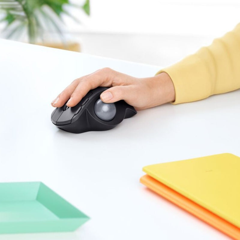 Person using Logitech MX ERGO PLUS trackball mouse on a white desk with colorful accessories