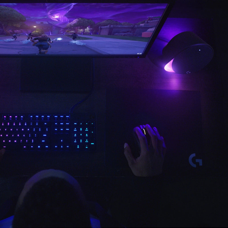 Logitech G560 speakers in a gaming setup showing purple LIGHTSYNC effects during gameplay