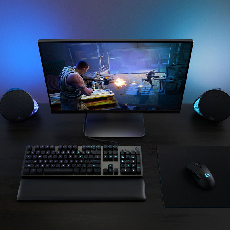 Gaming setup featuring Logitech G703 mouse with RGB keyboard and gaming monitor displaying action scene