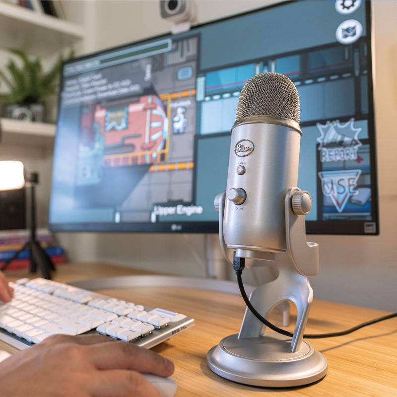 Blue Yeti microphone on desk with gaming setup and streaming software visible in background