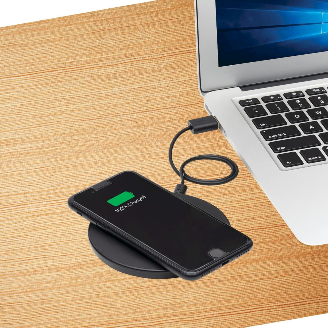 Tripp Lite wireless charger in use on wooden desk with laptop and phone showing 100% charge-alternate-image2