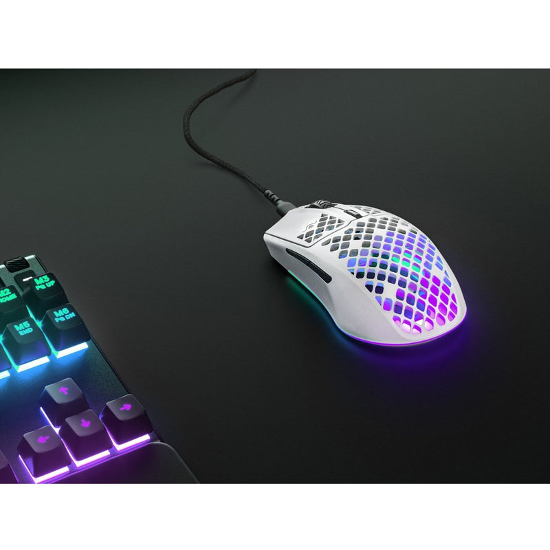 SteelSeries Aerox 3 Wireless mouse next to RGB gaming keyboard in dark setting