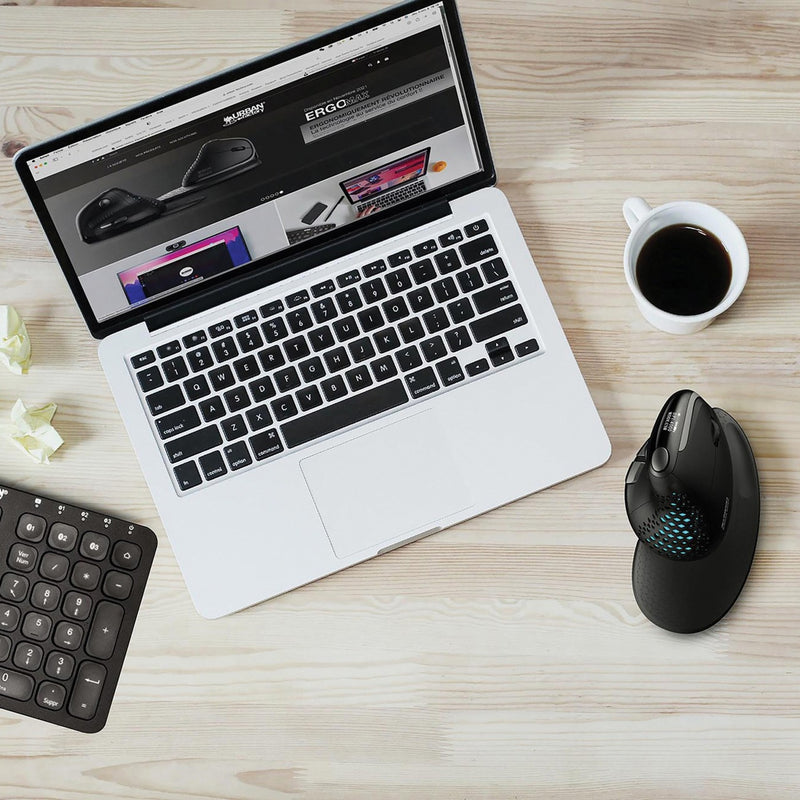 Lifestyle workspace setup showing ERGO MAX mouse alongside laptop, numeric keypad, and coffee cup on wooden desk