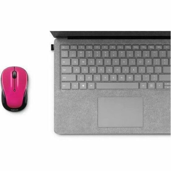 Logitech M325s red wireless mouse shown next to a laptop keyboard, demonstrating size and portability