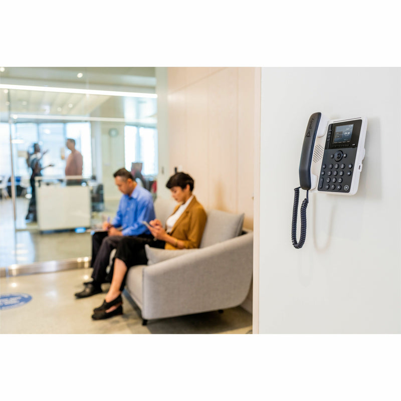 Poly Edge E100 IP phone mounted on office wall with business environment in background